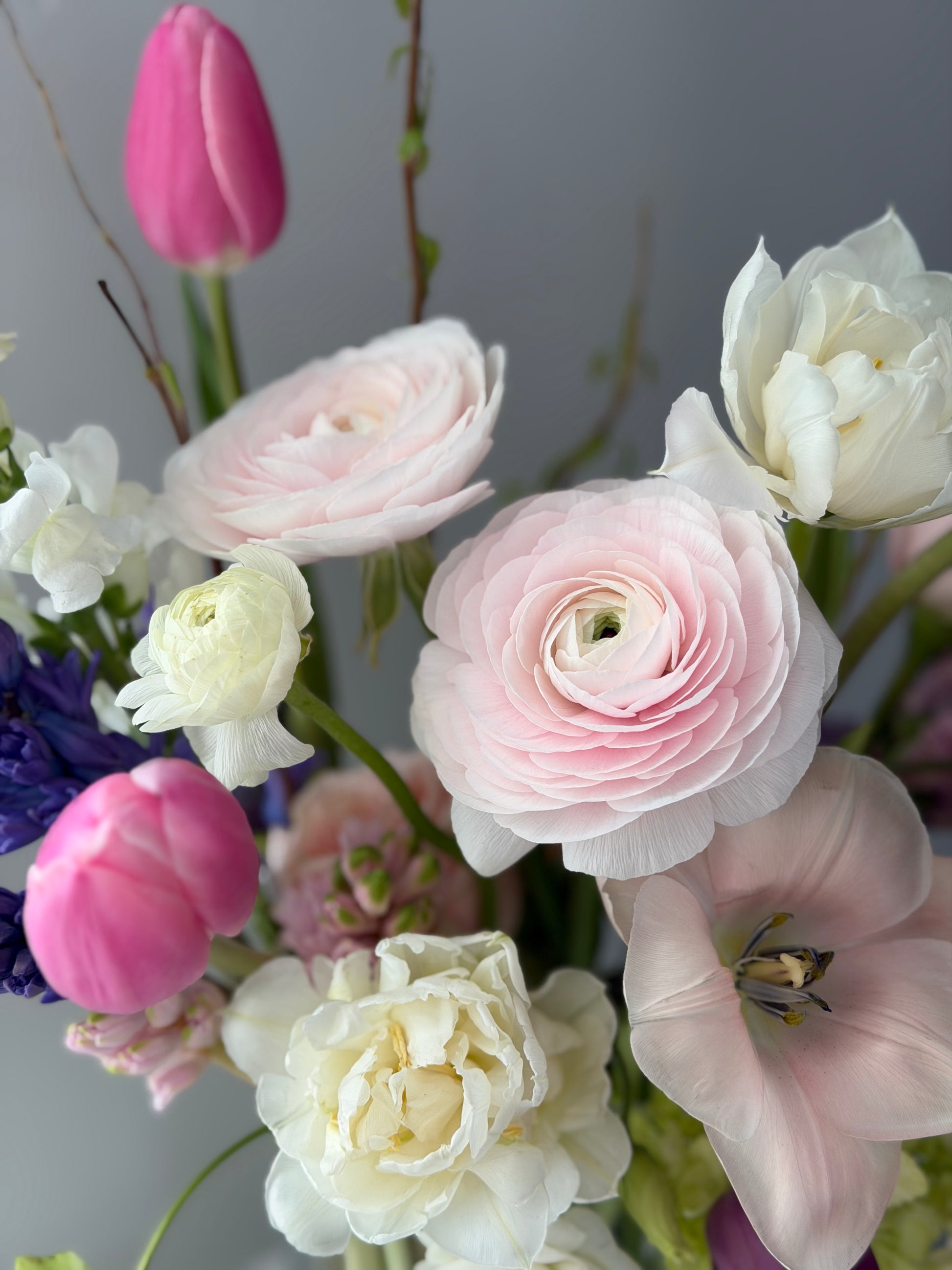 Close up of spring arrangement of pink, white, and purple flowers with a blurred gray background