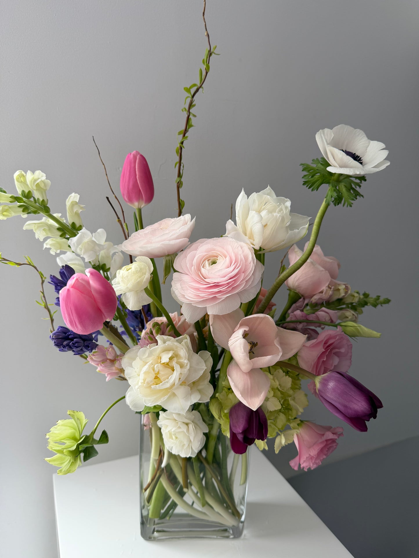 Lush spring flower arrangement in soft pink colours in a clear vase on a gray background